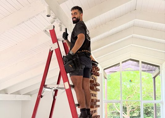 Quick Replace technician on a ladder installing ceiling fittings, giving a thumbs up