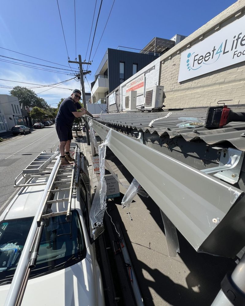 Tradesperson fitting a new gutter along a shop verandah