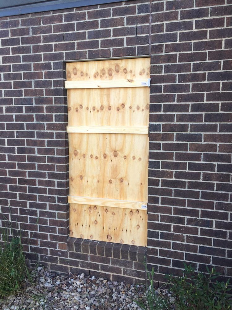 Broken window boarded up with plywood on a brick wall