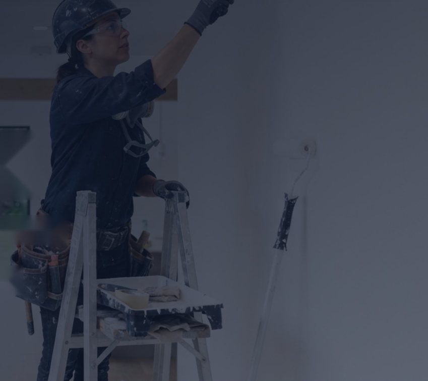 Painter in a hard hat painting a ceiling from a step ladder