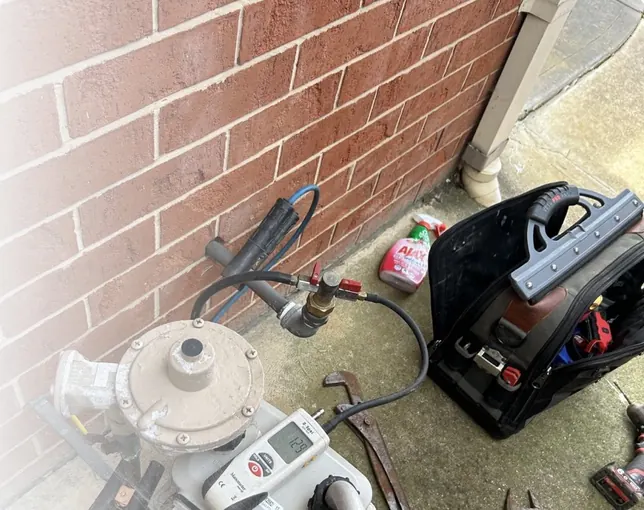Gas meter and regulator connection beside a brick wall