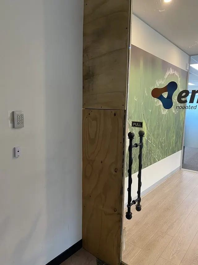 Broken glass panel beside an office door boarded with plywood