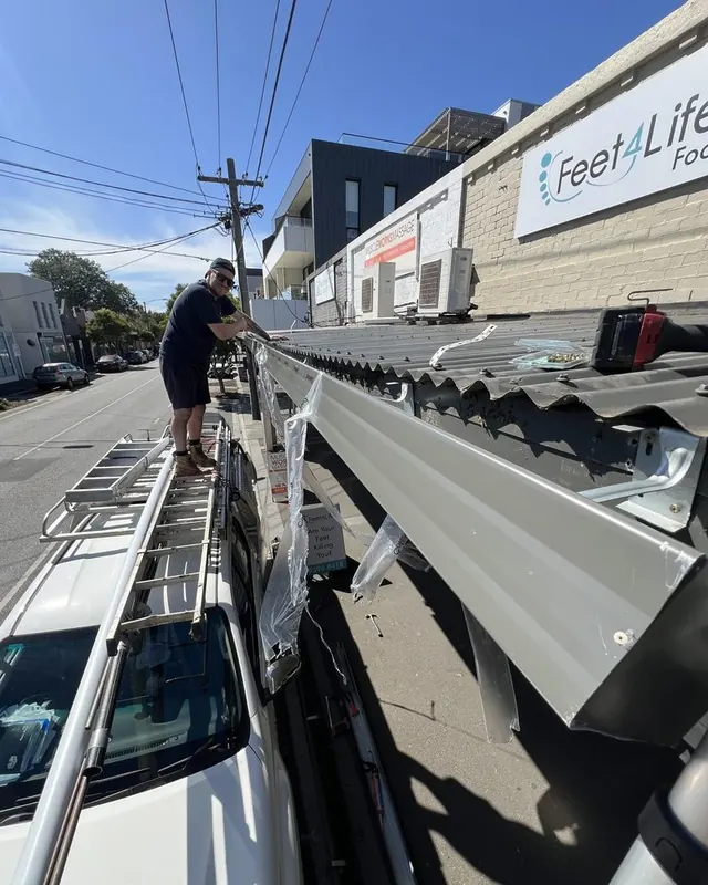 Tradesperson fitting a new gutter along a shop verandah