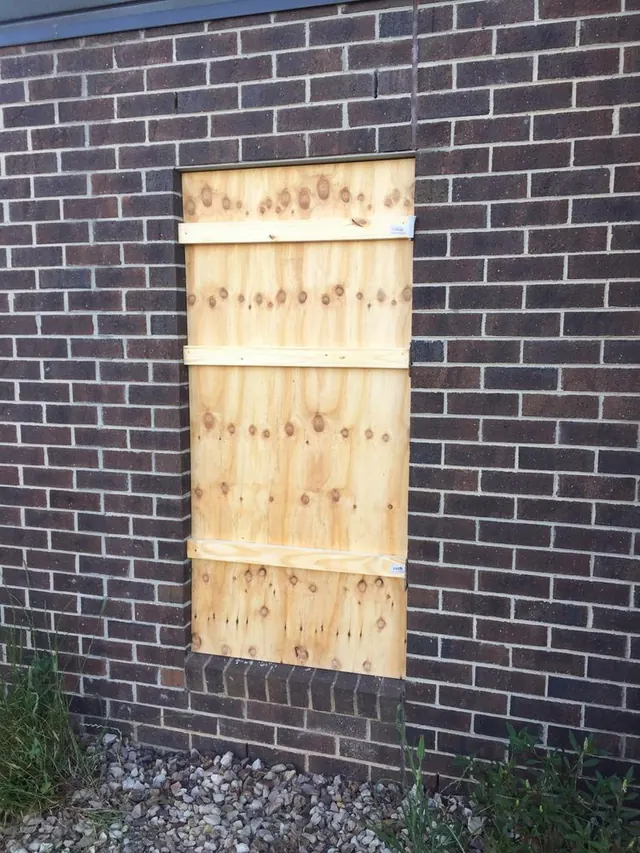 Broken window boarded up with plywood on a brick wall